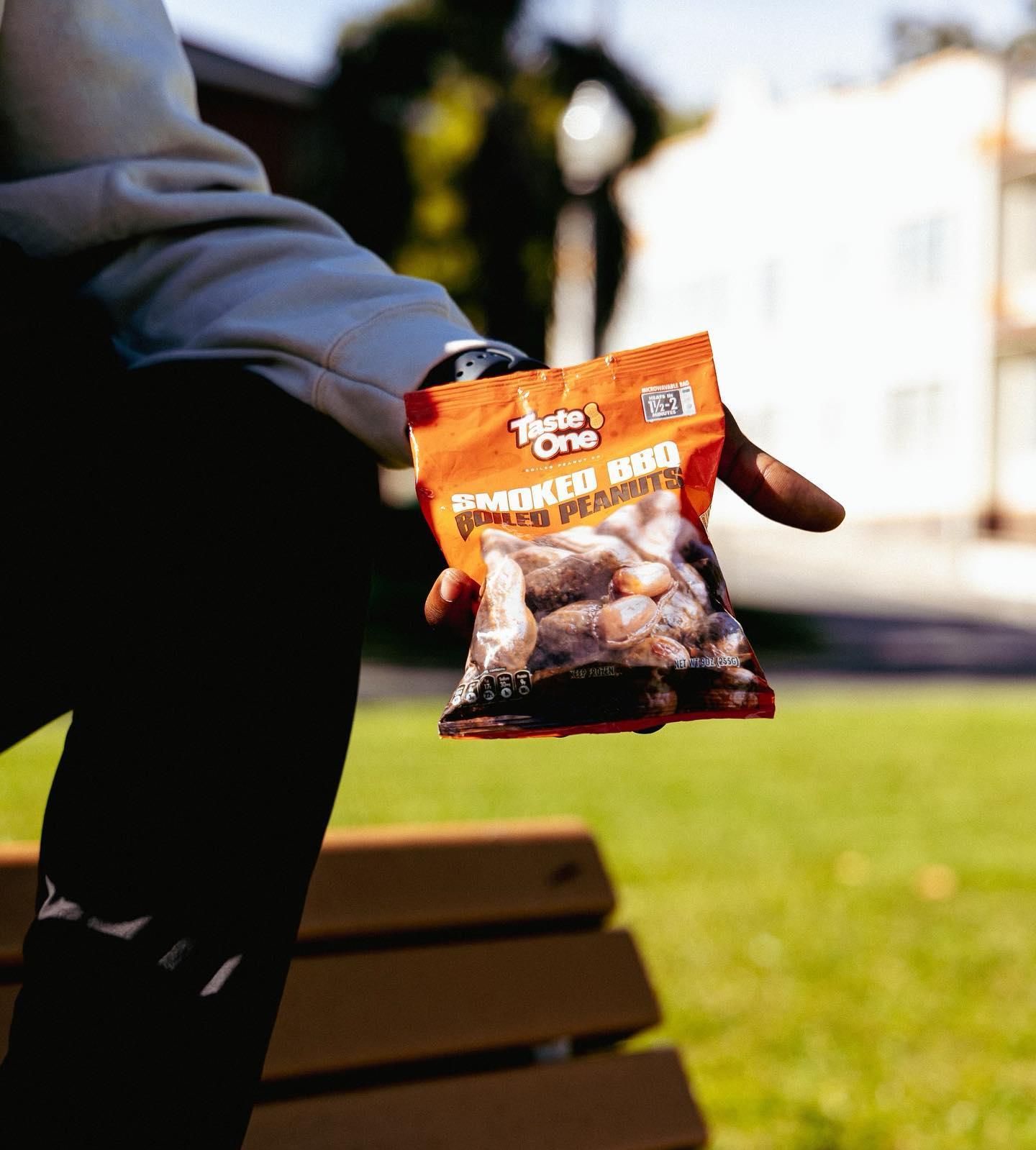 A real customer holding an open bag of Taste One Smoked BBQ Boiled Peanuts